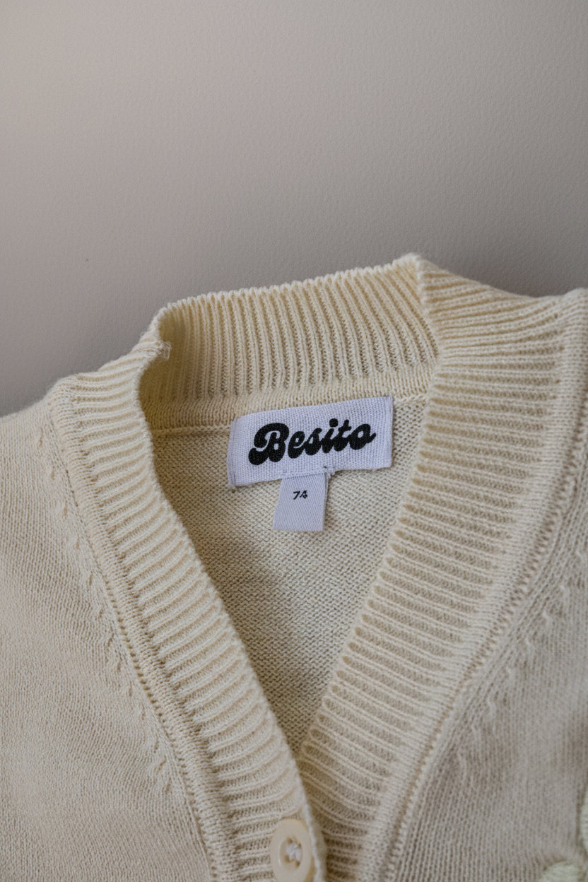 een detailfoto van de merino wollen cardigan in botergeel en met het logo